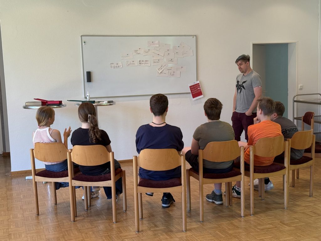 Lars Kokemüller steht neben einer Gruppe von Konfis vor einer Wand mit gesammelten Ideen und Szenen.