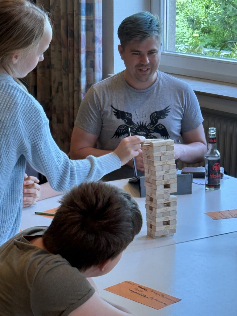 Lars Kokemüller sitzt mit mehreren Konfis an einem Tisch; gemeinsam spielen sie mit einem Holzturm.
