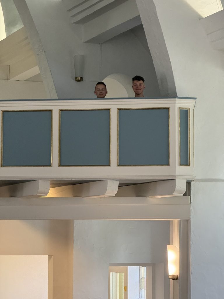 Zwei Mitglieder der Gruppe schauen von der Empore in den Kirchenraum.