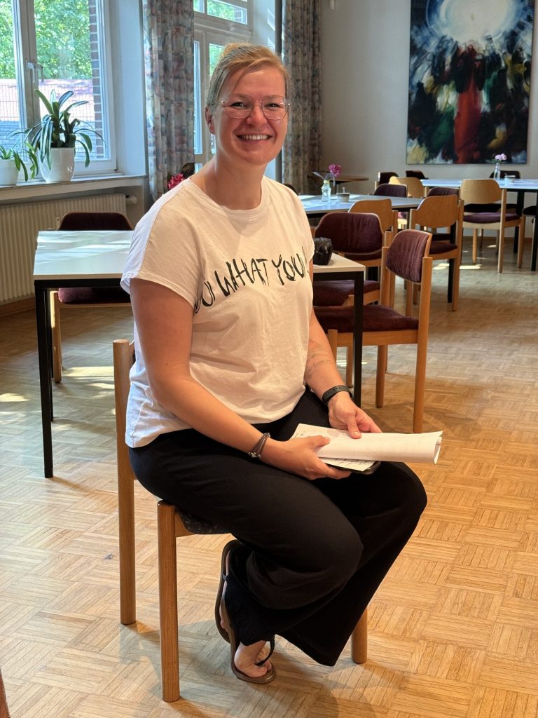 Ela Jackisch sitzt lächelnd mit Notizen in der Hand im Werkstattraum.