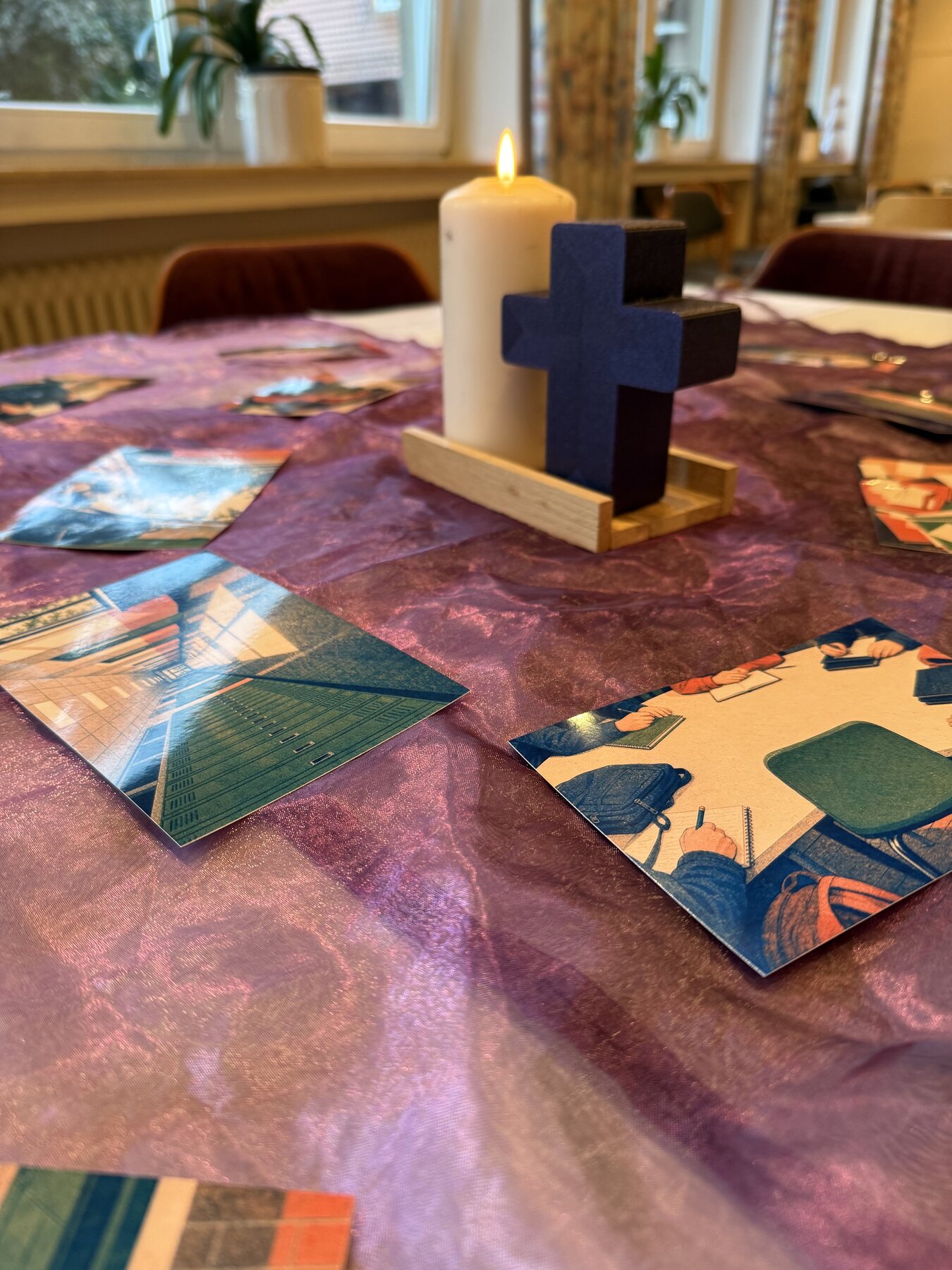 Auf einem violetten Tuch stehen eine Kerze und ein Kreuz zwischen ausgelegten Bildkarten.