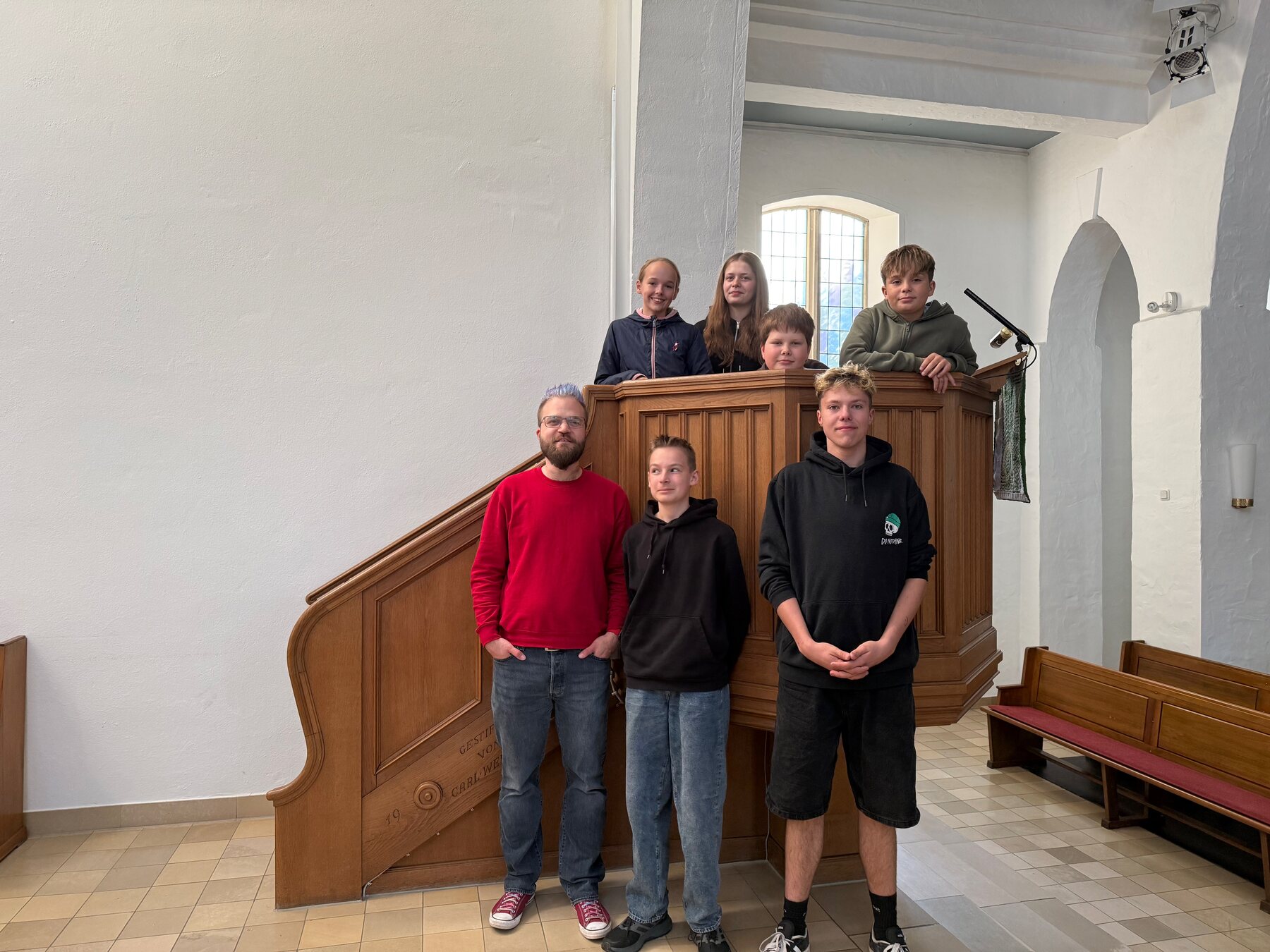 Christoph und sechs Konfis stehen an und vor der Kanzel der Apostelkirche.